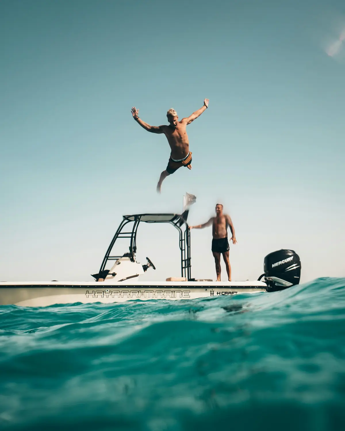 Friends jumping off a boat into turquoise water